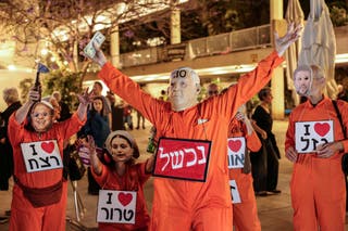 An Israeli left-wing activists wears a face mask depicting Israeli Prime Minister Benjamin Netanyahu and holding US dollars